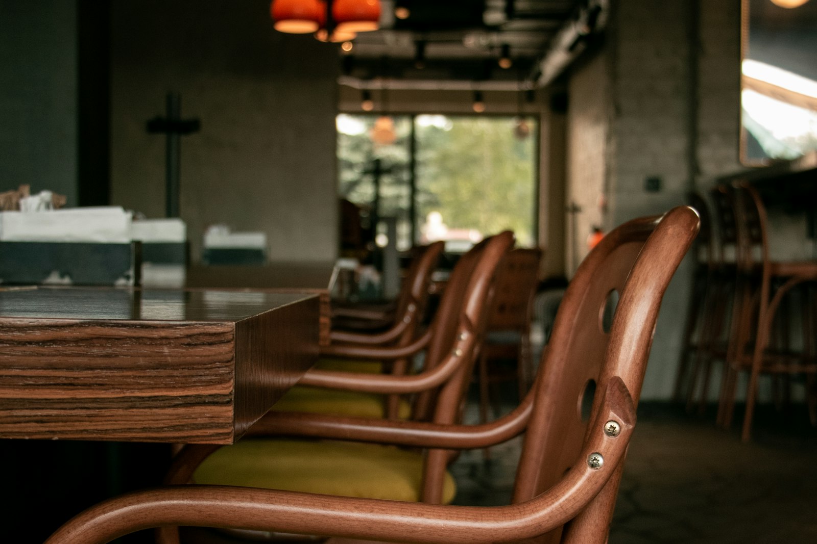 Alignement de chaises en bois et tables dans un café aux murs de brique